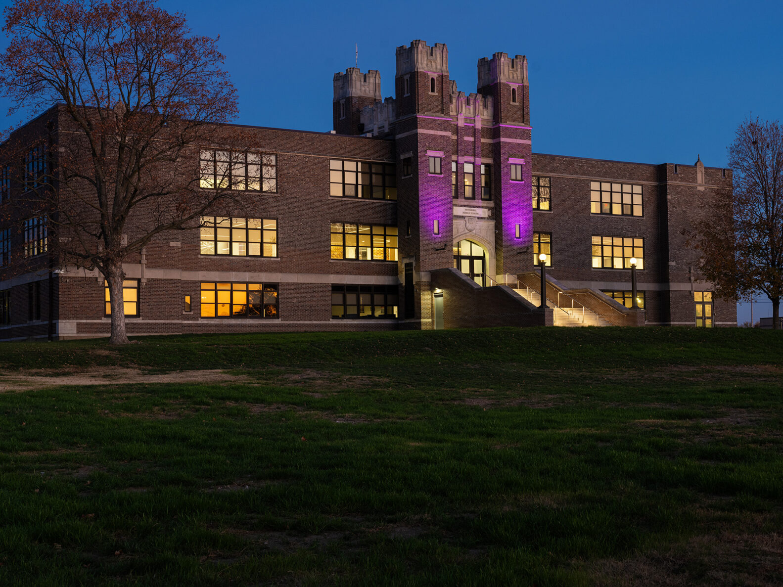 An exterior photo of Pittsburg Community Middle School at dusk with purple lights shining
